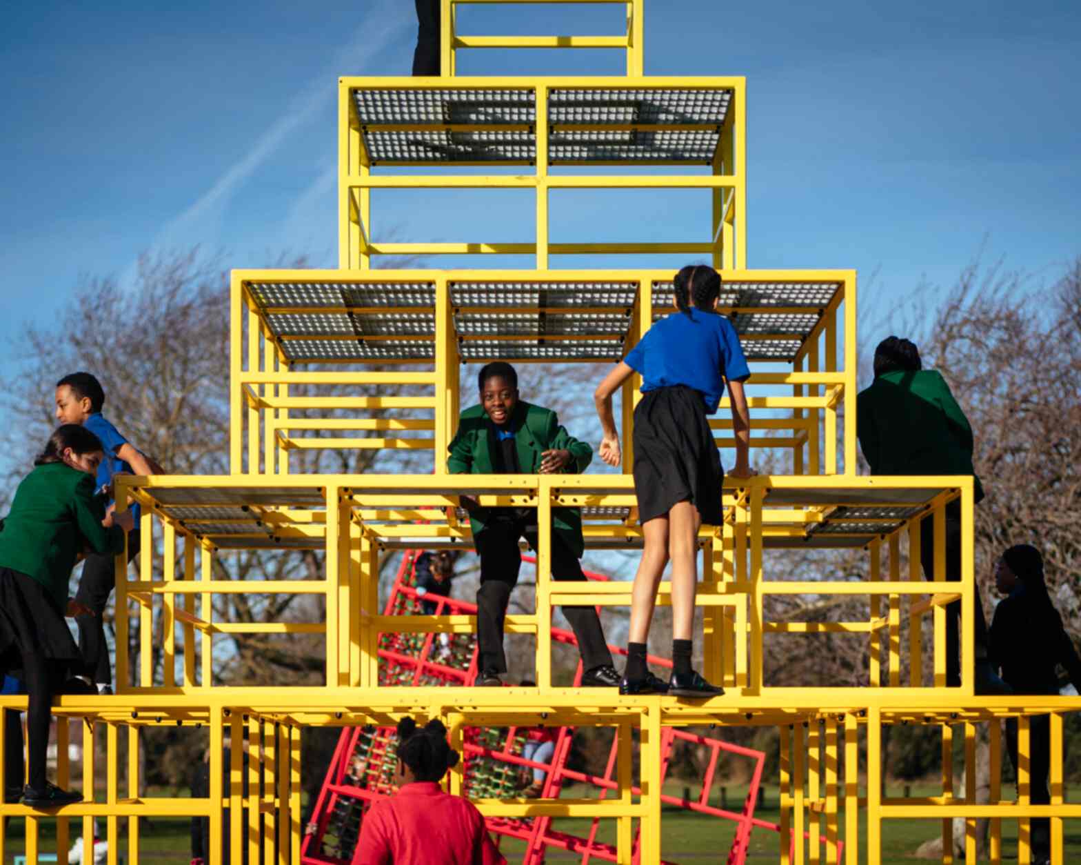 Photograph of the artwork: Eva Rothschild, 'Parsloes Memphis' playground. - Some children on a climbing frame which is the form of pyramid constructed from yellow tubular metal.