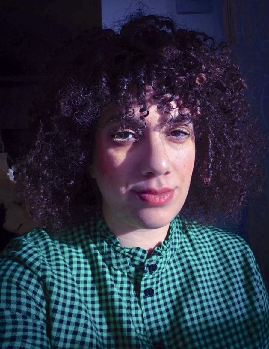 Maria Merzeban Portrait Photograph: Woman with Tighty curly brown hair, brown eyes, full lips, green checked shirt